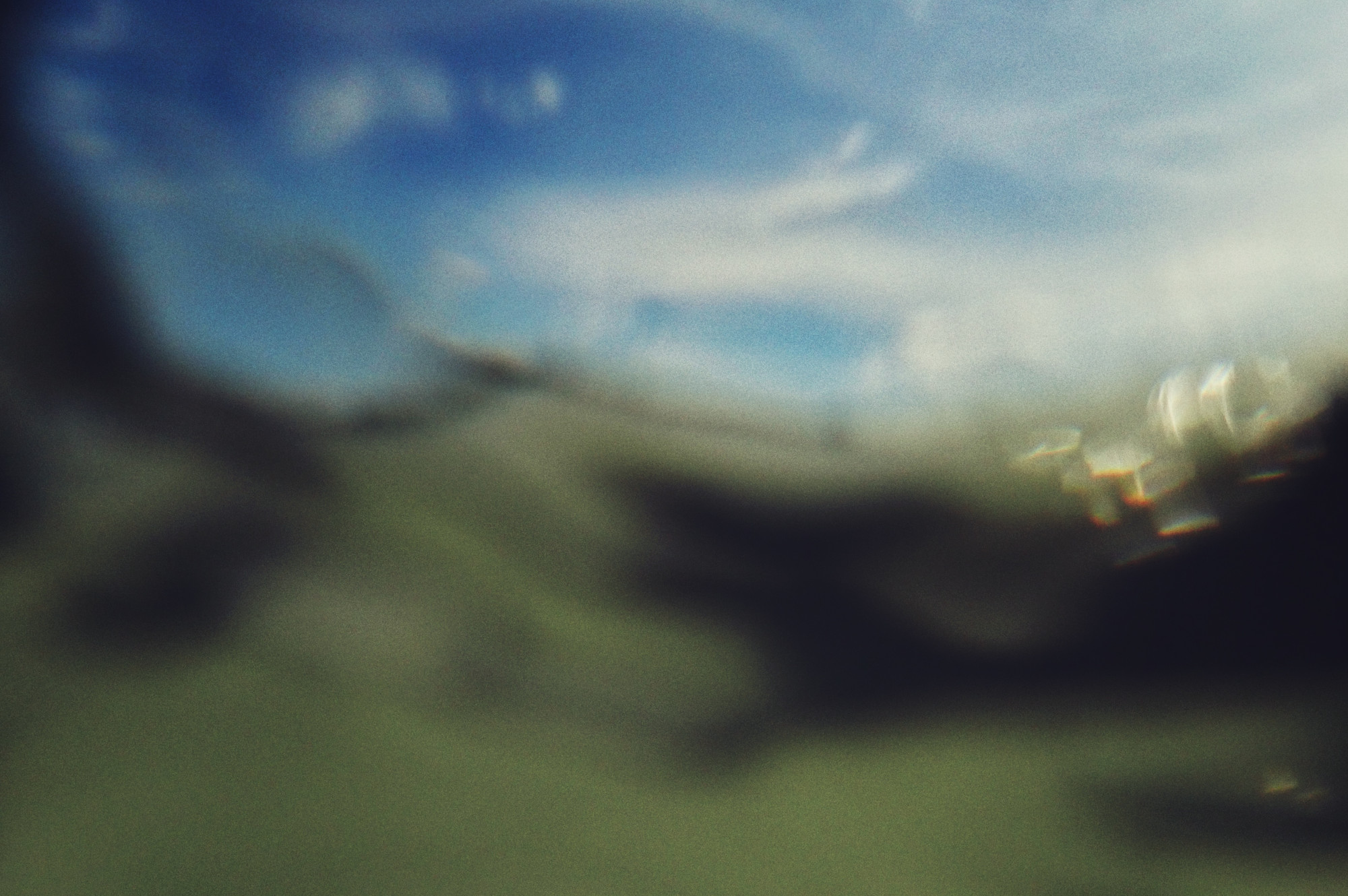 A horizontal colour photograph of sloshing water. The image is greenish, blurred and at an angle. It has been made from the water level. A spot of blue sky is visible on the right hand corner.