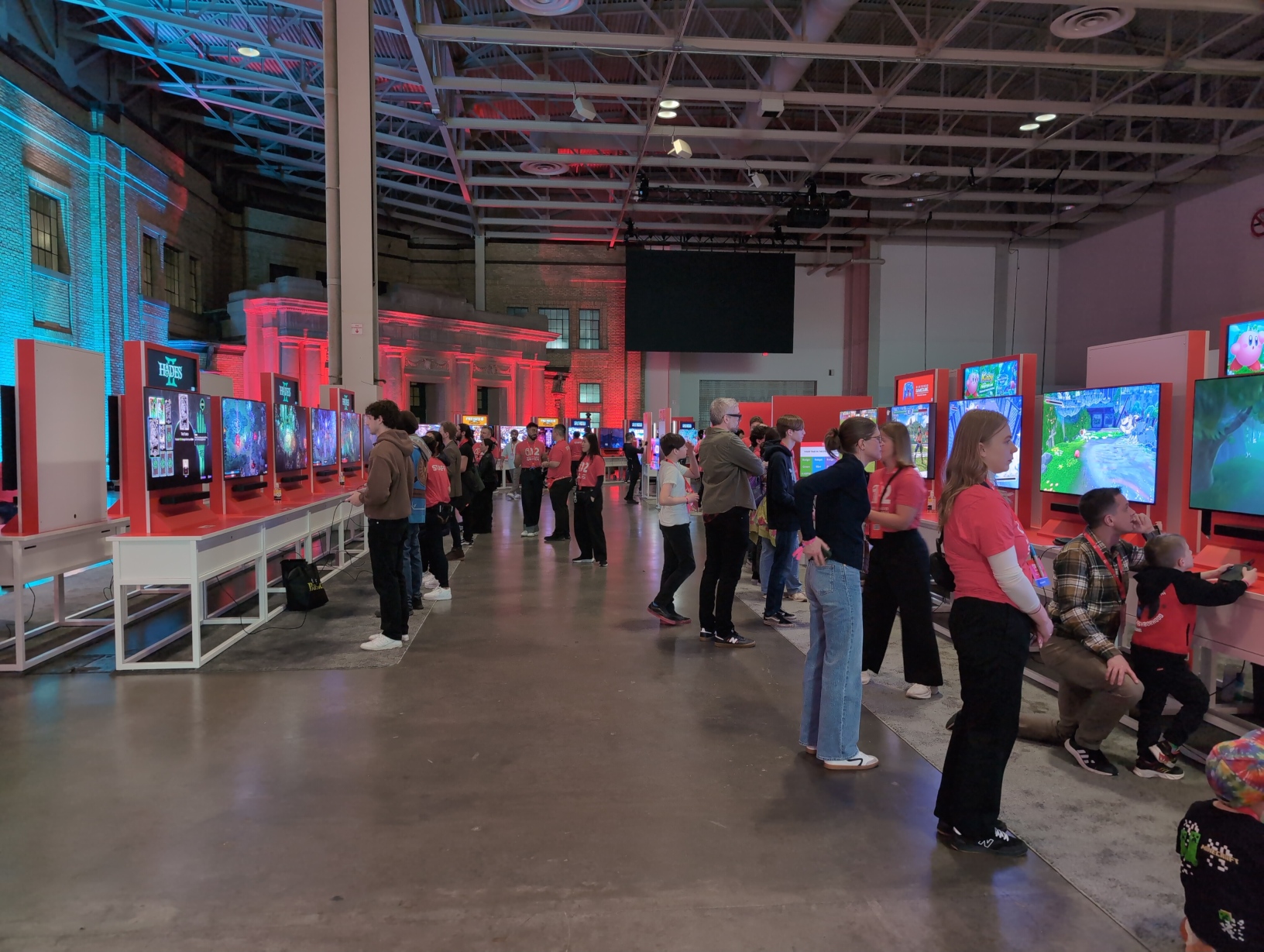 Photo looking between two long rows of TV setups. On the left, 6 setups for Hades II are visible, while on the right are 2 setups for Nintendo GameCube: Nintendo Classics setups and 4 more for Kirby and the Forgotten Land + Star‐Crossed World.