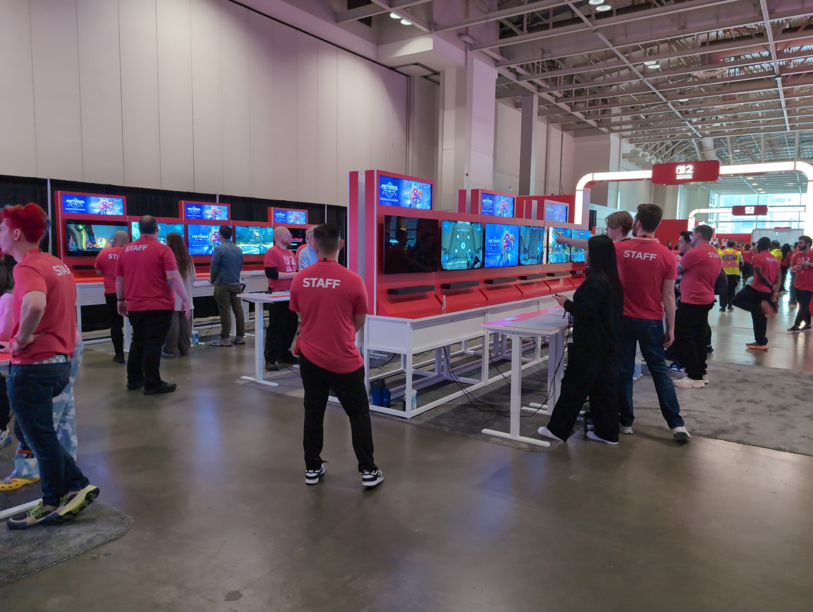 Photo facing the many Metroid Prime 4 setups. There are 3 rows of 6 setups, so 18 in total. Behind them are the gates between the mandatory exhibition areas.