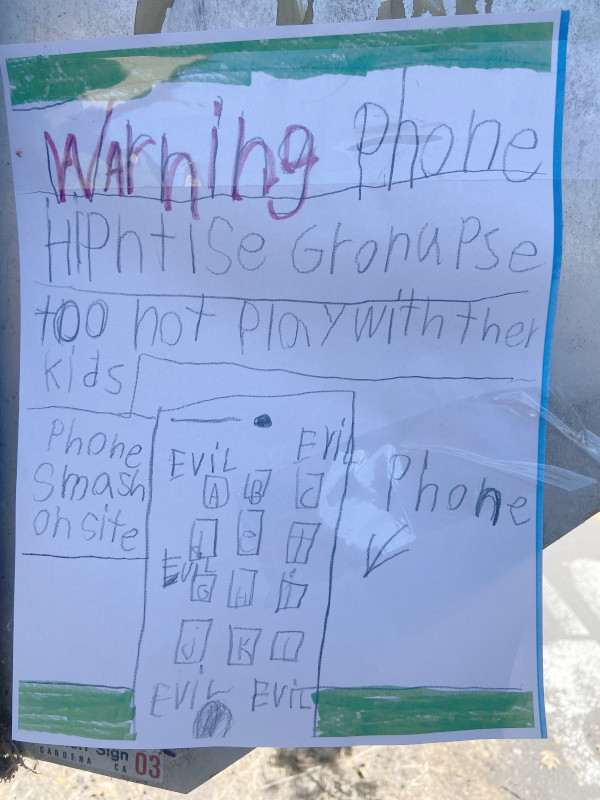 A handwritten sign reading "Warning Phone Hipntise Gronupse too not Play with ther kids. Phone smash on site. Evil Evil Evil Evil Evil <-- Phone"