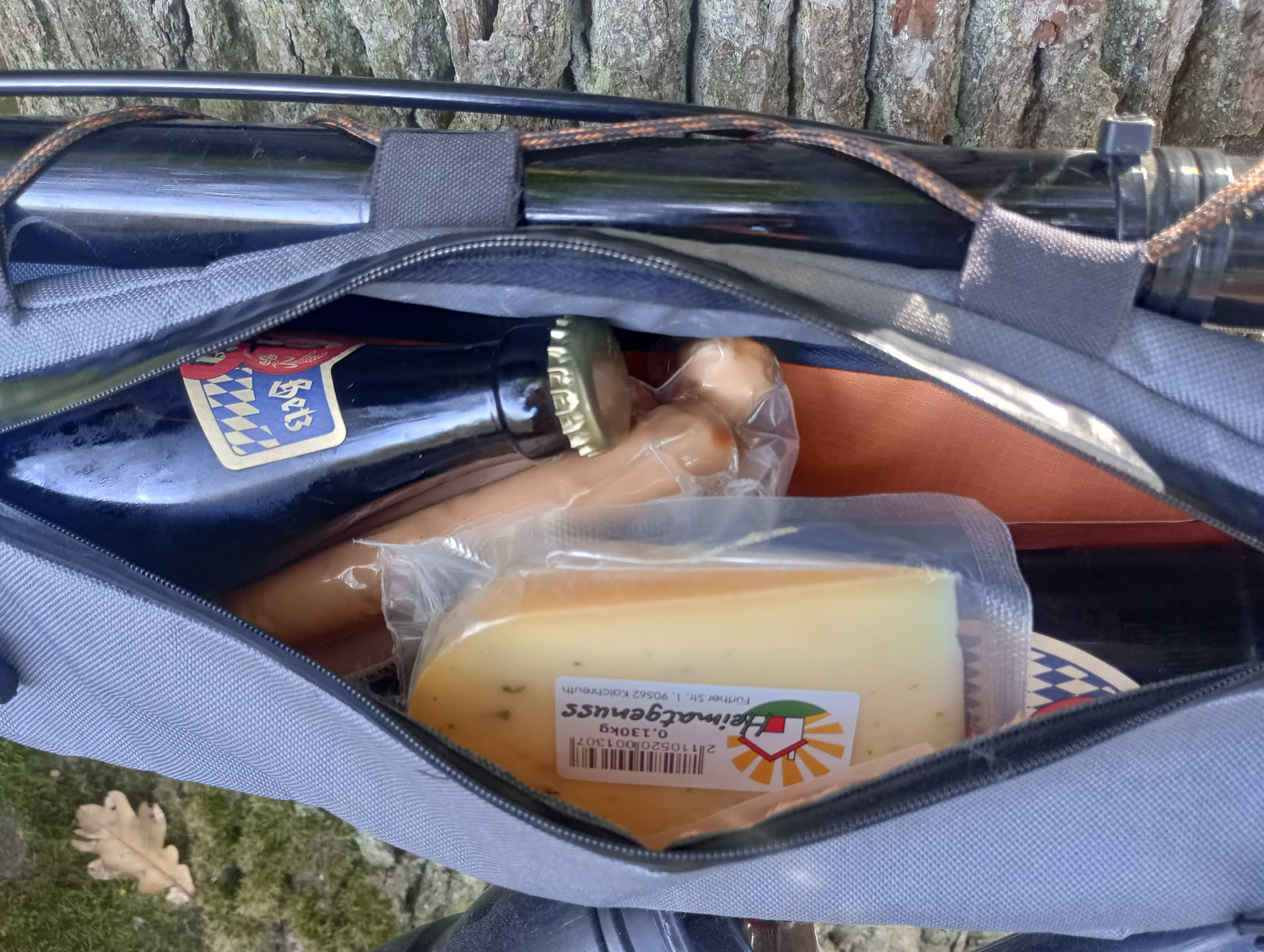 A photo of two beers, some sausage and cheese inside a bag attached to a bike frame. The sausages are for my dog.