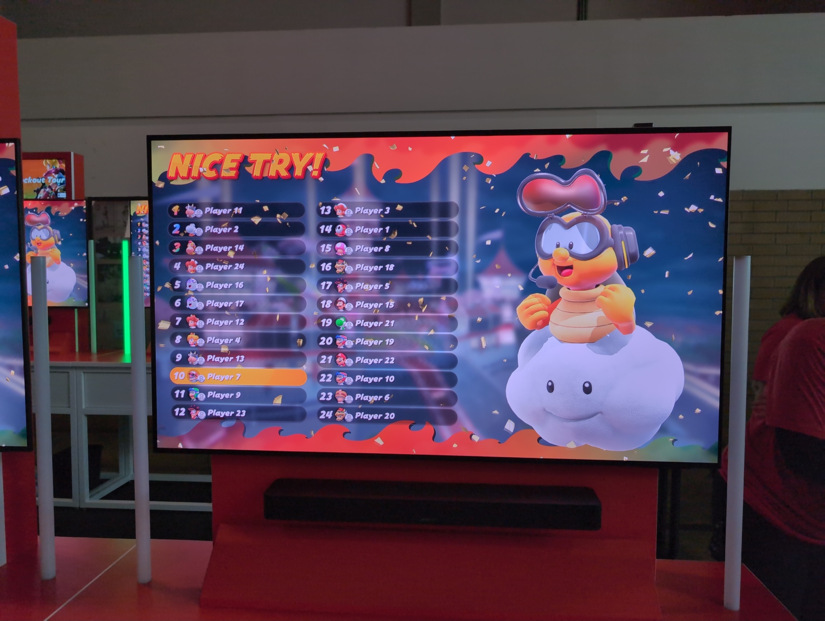 Photo of a TV showing a Knockout Tour results screen littered with falling confetti. Highlighted is biker Wario in tenth place out of 24; in first place is a cow. Above the player rankings are the words “NICE TRY!”