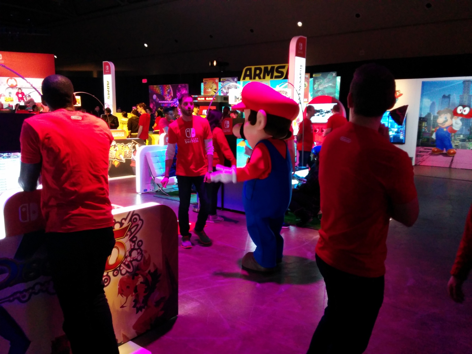 Photo of the Mario mascot walking around at the Nintendo Switch Preview Tour, surrounded by game setups, attendees, and staff.
