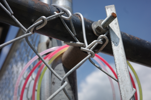 Photograph of colorful plastic bracelets hanging on a chain link fence