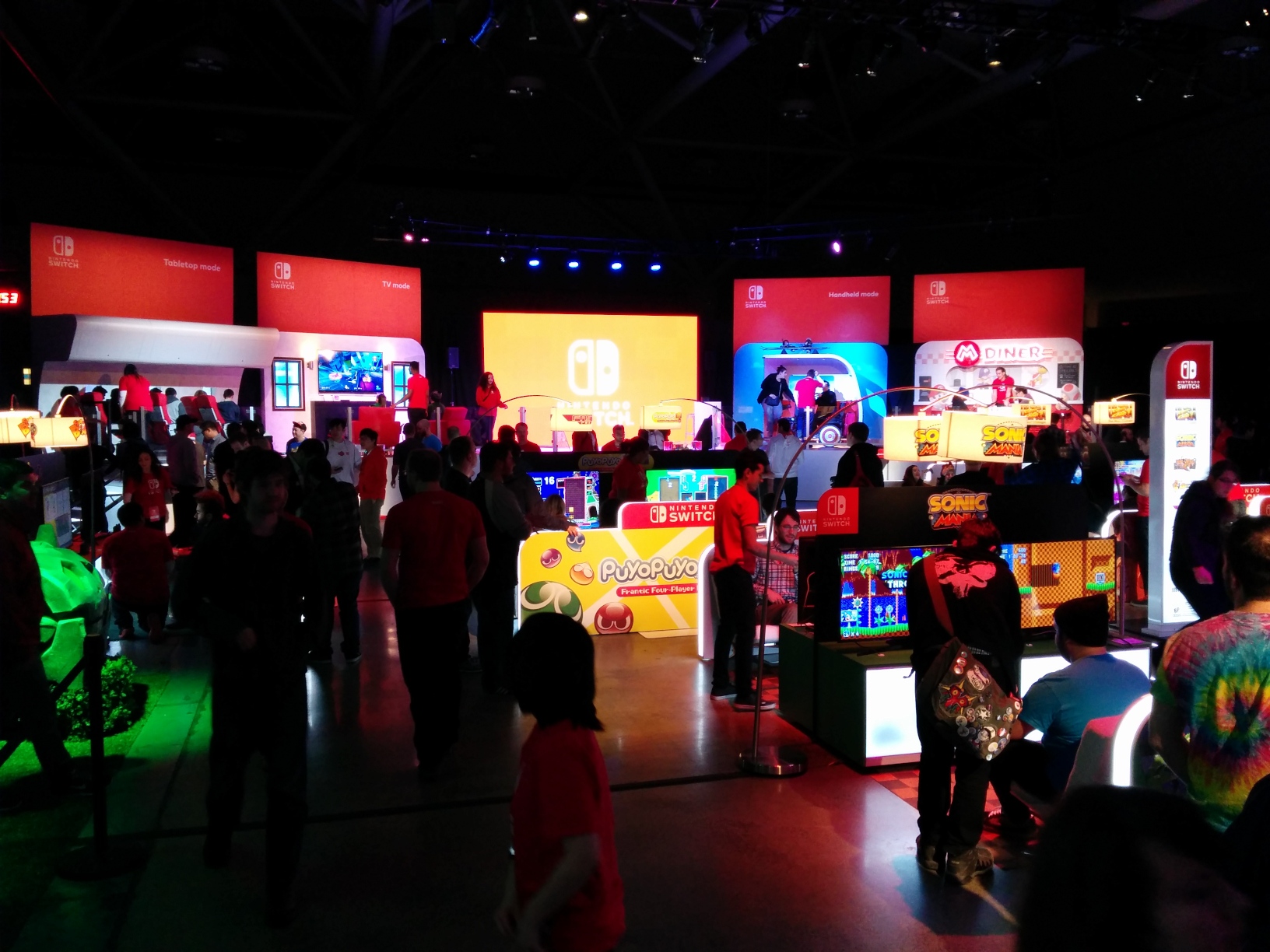 Photo facing the stage, with the aforementioned mock‐ups surrounding it partially visible from behind various game setups.